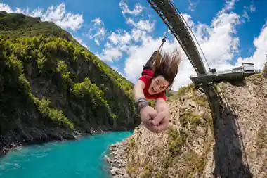 A jumper upside down below the bridge, hair falling, the river green behind