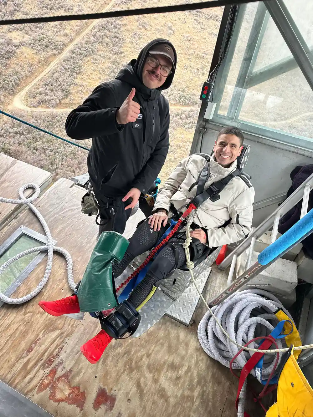 Two people in a cable car pod being harnessed by crew