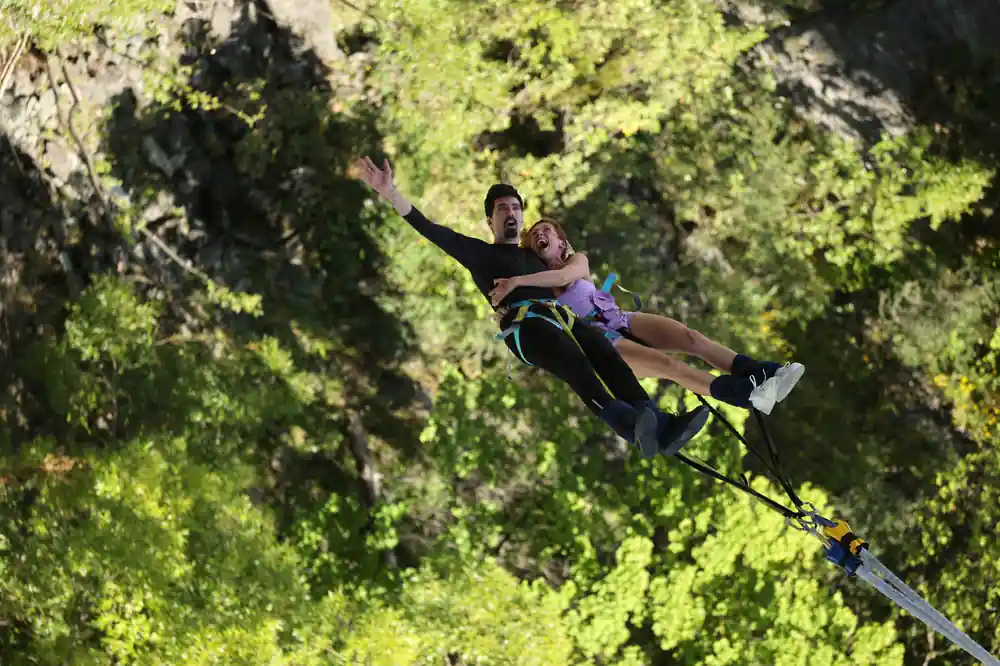 Two people jumping together in tandem above the trees
